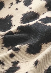 Tissu avec un fond beige présentant un motif vache noir et fauve, mettant en valeur une surface texturée avec des crêtes et des plis visibles.