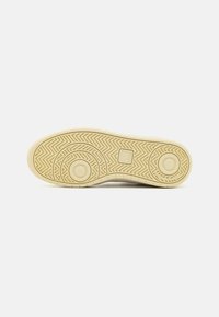 bézs gumi sneaker talp halszálka mintával, kör alakú díszítésekkel és texturált tapadásnövelő zónákkal; egy kis logó található a sarok közelében.