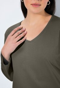 Olive green V-neck top made of soft fabric with long sleeves. Features a relaxed fit and visible stitching along the neckline.