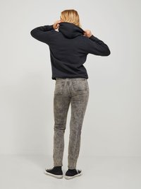 Felpa con cappuccio scura, jeans skinny grigi a motivi e sneakers nere. La felpa presenta un cappuccio e una vestibilità comoda. Jeans grigi strutturati.