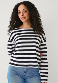 Zwart-wit gestreepte langemouwen shirt met een brede halslijn en een ontspannen pasvorm, gecombineerd met blauwe rechte spijkerbroek. Zachte katoen stof.
