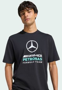 T-shirt noir en coton avec un grand logo Mercedes-Benz blanc et le texte "AMG PETRONAS FORMULA 1 TEAM" en blanc et vert menthe.