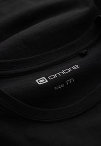 Mustat puuvillaiset T-paita pääntie, jossa on painettu valkoinen etiketti, jossa näkyy brändin nimi "ombre" ja koko "M".