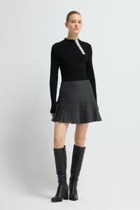 Zwart geribd langermig shirt met een textuurelement van kralen, gecombineerd met een grijze geplooide rok en kniehoge zwarte leren laarzen.