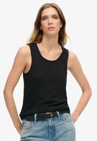 Zwarte mouwloze tanktop van lichtgewicht stof, met een ronde halslijn en subtiele branding op de borst. Gecombineerd met denim shorts.