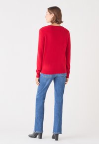 Maglione rosso con maniche lunghe e scollo rotondo, abbinato a jeans blu a gamba dritta e stivaletti neri con tacco. Texture liscia.