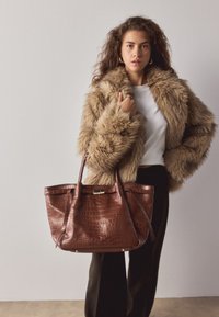 Sac fourre-tout en cuir marron à motif crocodile avec doubles poignées ; comporte un accent doré près du haut et des pieds en métal à la base pour la stabilité.