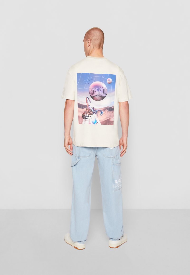 Cream-colored t-shirt with a graphic print on the back, paired with light blue baggy pants and white sneakers.