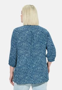 Blusa floreale blu scuro con maniche a 3/4, vestibilità ampia, dettaglio della piega sul retro e un delicato motivo blu chiaro su tessuto leggero.