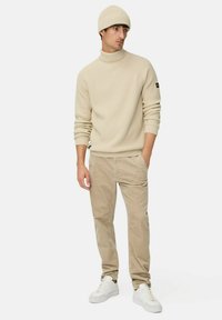 Beige gestreifter Rollkragenpullover kombiniert mit beige Kordhosen und weißen Turnschuhen; das Modell trägt eine passende Mütze; lässiger Look.