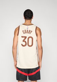 Vīriešu basketbola krekls gaiši bēšā krāsā ar brūniem akcentiem. Aizmugurē drukāts uzvārds "CURRY" un numurs "30". Viegls auduma dizains.