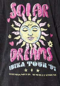 Yellow sun with a serene face, surrounded by pink flames, pink hearts, stars, and flowers, with text "Solar Dreams Ibiza Tour '97" on black background.