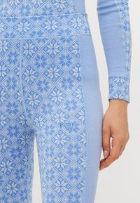 Close-up de uma pessoa a usar leggings estampadas em azul claro e uma blusa de mangas longas combinando com desenhos geométricos de flocos de neve.