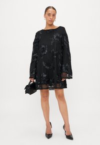 Melna kleita ar garām piedurknēm, ziedu izšuvumiem, caurspīdīgu audumu un brīvu piegriezumu. Saskan ar melniem papēžiem un mazu rokassomu.