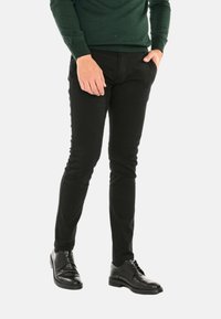 Pantaloni neri slim-fit realizzati in tessuto morbido, con tasche laterali e abbinati a scarpe eleganti nere lucide.