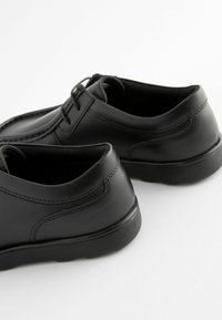 Chaussures en cuir noir avec une finition lisse, un bout rond et des détails de couture minimaux. Elles disposent d'une semelle en caoutchouc pour l'adhérence et la durabilité.