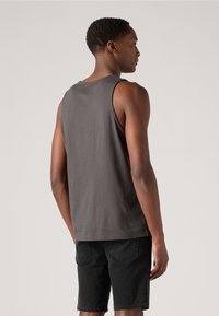 Débardeur en coton gris foncé avec une coupe décontractée, un col rond et une conception sans manches. Associé à un short en denim noir.