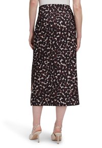 Midikleid in dunkelbrown und cremefarbenem abstraktem Muster, mit geradem Schnitt und seitlichen Schlitzen, kombiniert mit beigen High-Heels.