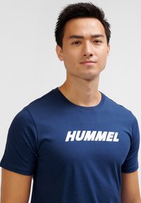 Marinblå bomullst-shirt med rund hals och korta ärmar, med ett framträdande vitt "HUMMEL"-tryck över bröstet.