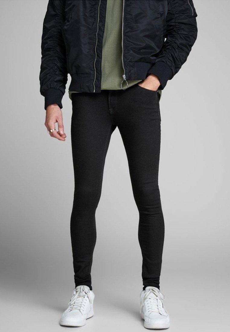 Pantalones vaqueros ajustados negros, confeccionados en denim, con un diseño elegante y una textura suave, combinados con una camisa verde y una chaqueta bomber negra.