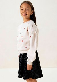 Lichtgrijze sweatshirt met kleurrijke borduursels van sterren, harten en een maan, gecombineerd met een zwarte rok met pailletten. Korte pofmouwen en ribgebreide boorden.