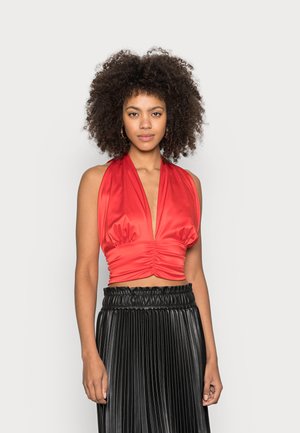 Top curto halter de cetim vermelho com detalhe franzido na frente, combinado com uma saia plissada preta com cintura elástica.