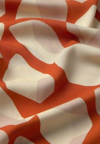 Textília so zaujímavým abstraktným vzorom nepravidelných, organických tvarov v oranžovej a svetlej béžovej farbe, s hladkou, matnou textúrou.