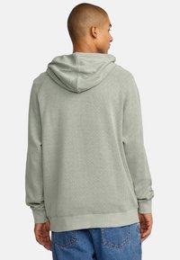 Groene gebreide hoodie met een geribbelde textuur, verstelbaar trekkoord en een relaxte snit. Voorzien van elastische manchetten en een stevige zoom.