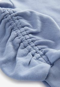 Tela de sudadera de color azul claro con textura recogida y puños acanalados, que enfatizan la suavidad y el ligero brillo del material.