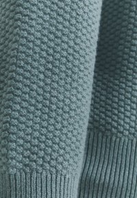Maglione lavorato a maglia in morbido e tenue blu teal. Presenta un motivo a pallini in rilievo con polsini e orlo a coste, realizzato con un filato spesso.