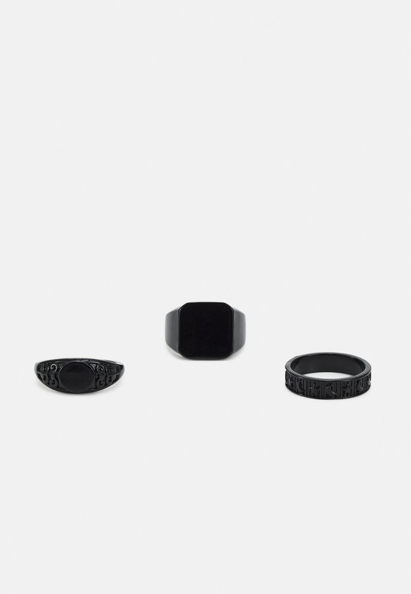 Três anéis pretos: um com detalhes ornamentados, um octagonal e liso, e um terceiro com uma banda texturizada com padrões.