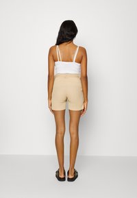 Beige, teksturerte shorts med tett liv og sidelommer, paret med en hvit tanktop. Modellen ses bakfra.