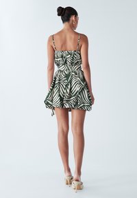 Zaļas krāsas kleita ar baltu lapu rakstu, pieguļošs korsete, izplešanās svārki, regulējamas smalkas lencītes un piesaista pie vidukļa.