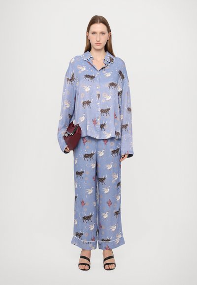 Set de pijamale cu imprimeu albastru, format dintr-o cămașă cu butoane și pantaloni largi, decorat cu modele celestiale și animale, completat cu sandale negre cu bretele.