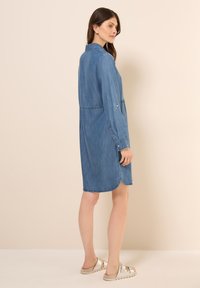 Robe chemise en jean bleu moyen, dotée d'un col, de manches longues avec des poignets boutonnés et d'un ourlet arrondi avec des fentes latérales pour faciliter le mouvement.