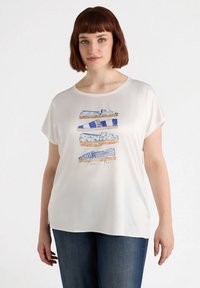 Top blanco de manga corta con un diseño impreso de zapatos azules en varios patrones. La tela tiene una textura suave y lisa.