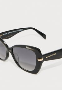 Mustad mustangad läikiva raamiga, hallide läätsede ja kuldsete detailidega. Brändi nimi "Michael Kors" on nähtav templitel.