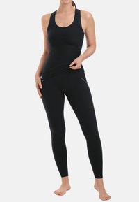 Zwarte sportieve tanktop en leggings van rekbare stof. De tanktop heeft brede banden; de leggings hebben zijzakken met rits.