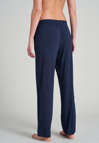 Pantalones de chándal azul marino con una textura suave y lisa. Cuentan con una cinturilla elástica y un corte relajado que llega hasta los tobillos.