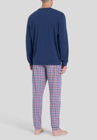 Maglietta a maniche lunghe blu navy con collo a giro abbinata a pantaloni del pigiama a quadri rossi e blu in tessuto morbido. I piedi sono nudi.