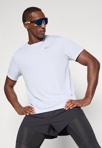 Nike könnyű, rövid ujjú, világosszürke sportpóló, kis logóval, fekete rövidnadrággal és sportos kék napszemüveggel párosítva.
