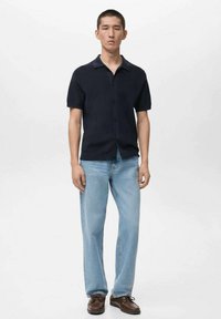 Camicia blu navy a maniche corte con bottoni, dalla texture morbida, abbinata a jeans a gamba dritta azzurri e scarpe marroni stringate.