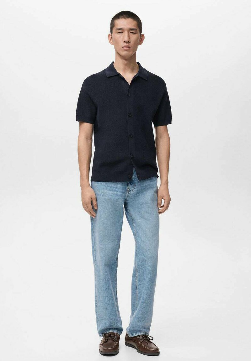 Marineblaues kurzärmeliges Hemd mit Knöpfen und weicher Textur, kombiniert mit hellblauen gerade geschnittenen Jeans und braunen Schnürschuhen.