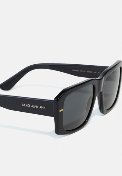 Ochelari de soare rectangulari negri cu lentile întunecate. Ramele au un finisaj lucios și un accent subtil de aur pe laturi. Logo-ul brandului este imprimat pe braț.