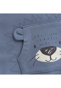 Weiches blaues Gewebe mit einem Design eines Tiergesichts und gestickten Akzenten. Inklusive einer kleinen Tasche mit einem 3D-Ohrdetail.