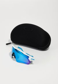 Sport sunglasses with blue gradient lenses and white accents, placed next to a black oval hard case with a zipper.