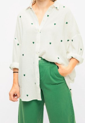 Hvid skjorte med grønne hjerte mønstre, lavet af tekstureret stof, parret med grønne bukser med en sidelomme.