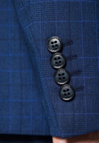 Granatowa marynarka z teksturowanej tkaniny, wyróżniająca się subtelnym wzorem w kratę. Cztery czarne guziki na mankiecie, oznaczone "LANERTO."