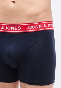 Μπλε ναυτικό βαμβακερά μπόξερ briefs με κόκκινη ελαστική ζώνη μέσης που φέρει λευκή επιγραφή "JACK & JONES" και εφαρμοστή σχεδίαση.
