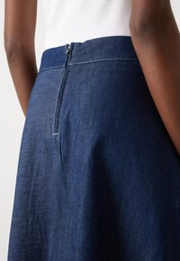 Temno modra denim krila z oprijetim pasom, skrito zadrgo, rahlim šivom in gladko teksturo.